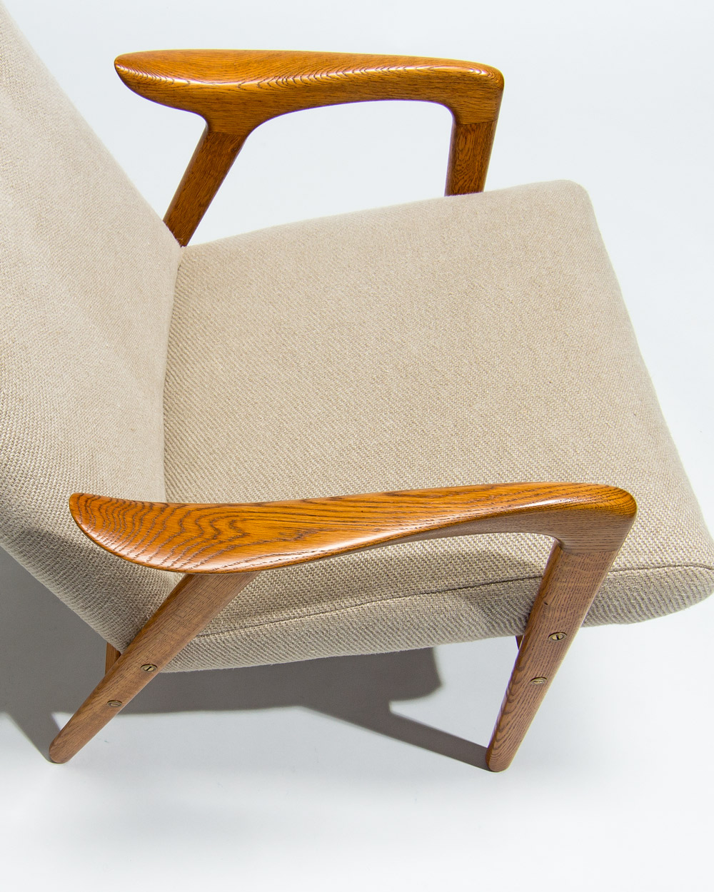Close detail of sculpted oak armrest and linen seat on Yngve Ekstrom lounge chair